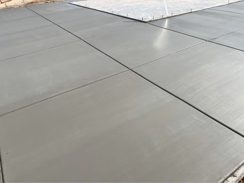 Freshly poured and smoothed concrete slabs with visible expansion joints, forming a grid pattern. The surface has a matte finish, showcasing the quality of premium concrete services in Yucaipa CA. The surrounding area highlights part of a construction site with additional materials managed by licensed concrete contractors.