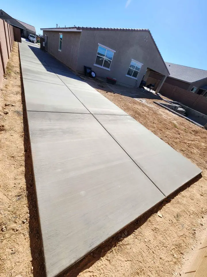 A freshly paved concrete path, courtesy of Berdoo Concrete, leads to a modern house with a brown exterior. The path is surrounded by dirt and appears to be a new addition to the property. The sky over Loma Linda is clear and blue, indicating a sunny day.